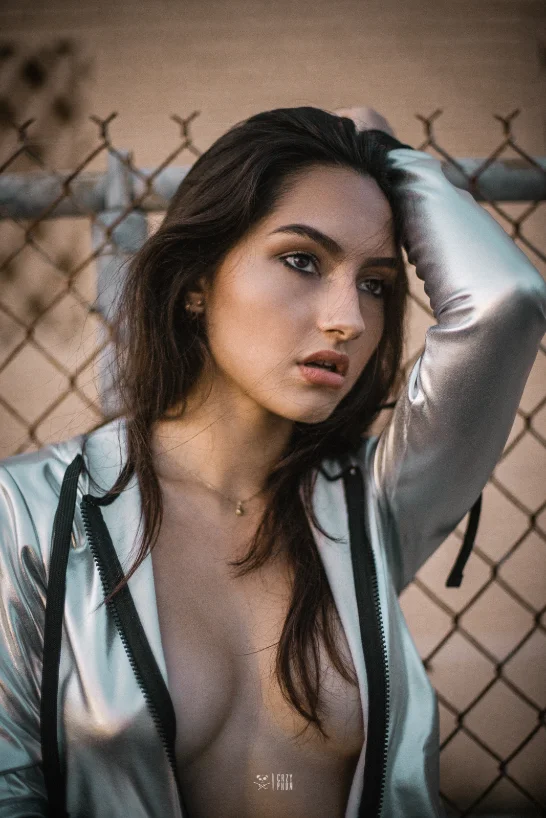 Model in a silver jacket against a chain-link fence at dusk — Faces series by CRZYPNDA