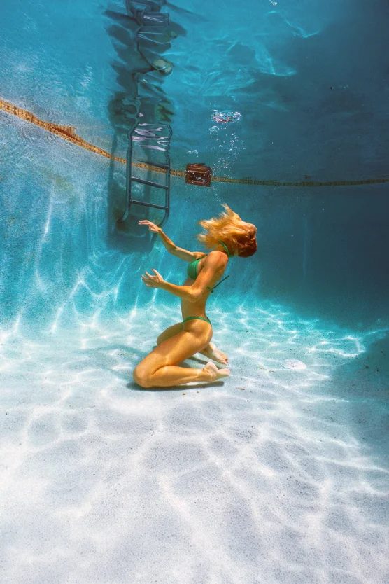Kneeling figure in a green bikini on a sunlit pool floor — CRZYPNDA underwater photography